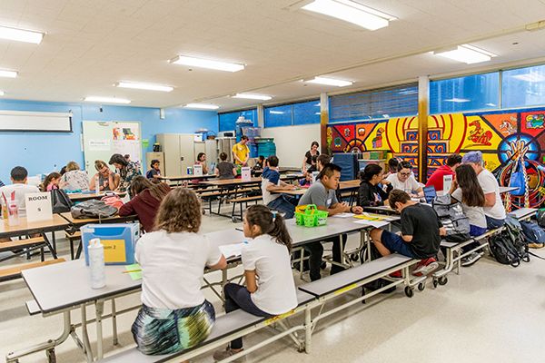 A room of long tables with groups of kids engaged in their work